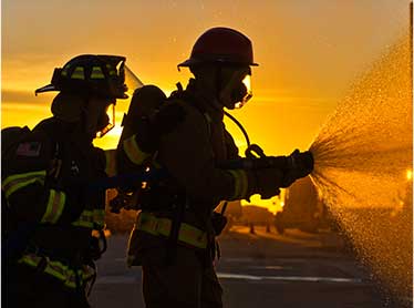 Two Fireman using a fire hose to take out a fire as the sunset goes down.