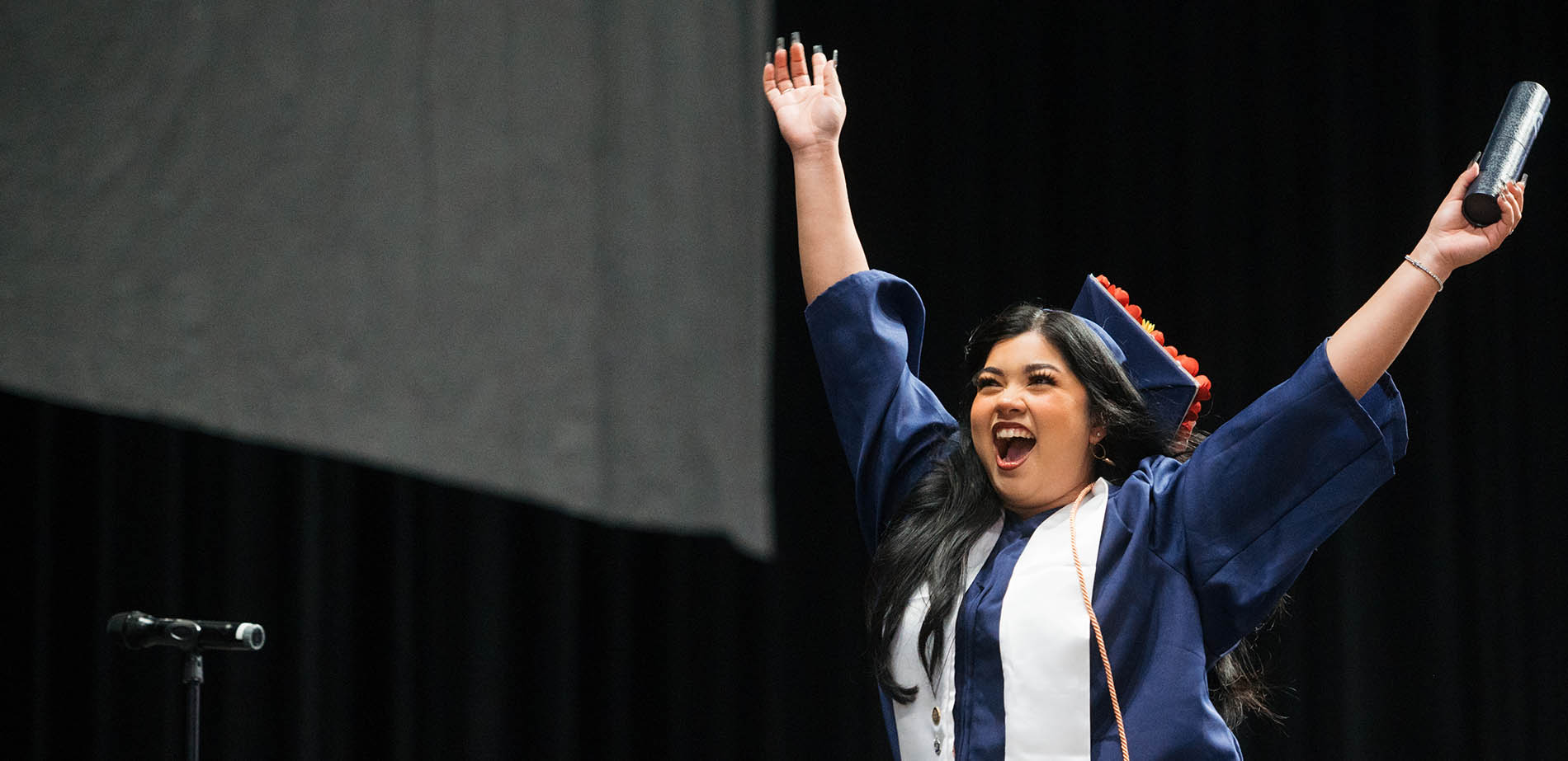 A Del Mar College graduate raising her arms happily at graduation