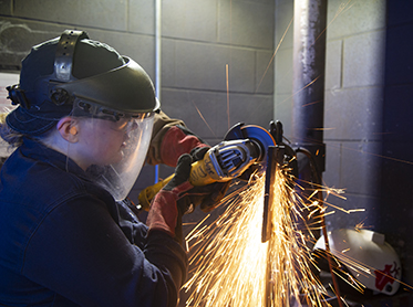 Sparks fly while a student wearing safety gear welds pipe