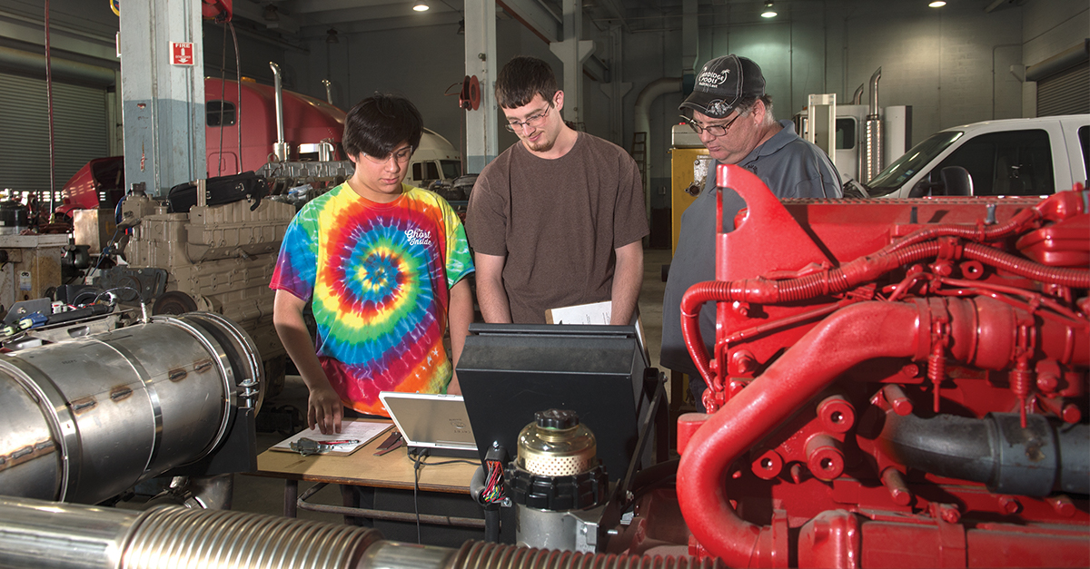 A diesel technician looking at the diagnostics of an engine from a laptop.