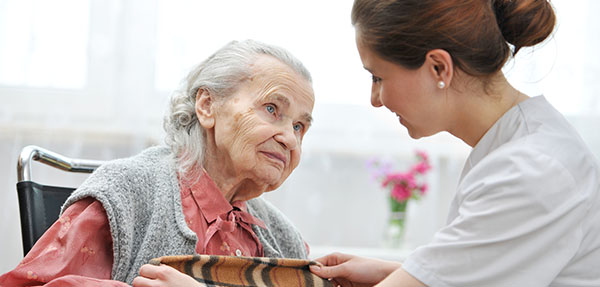 A student nurse gives an elderly woman a blanket.