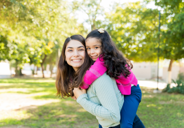 Happy female student with her daughter on her back looking at the camera.