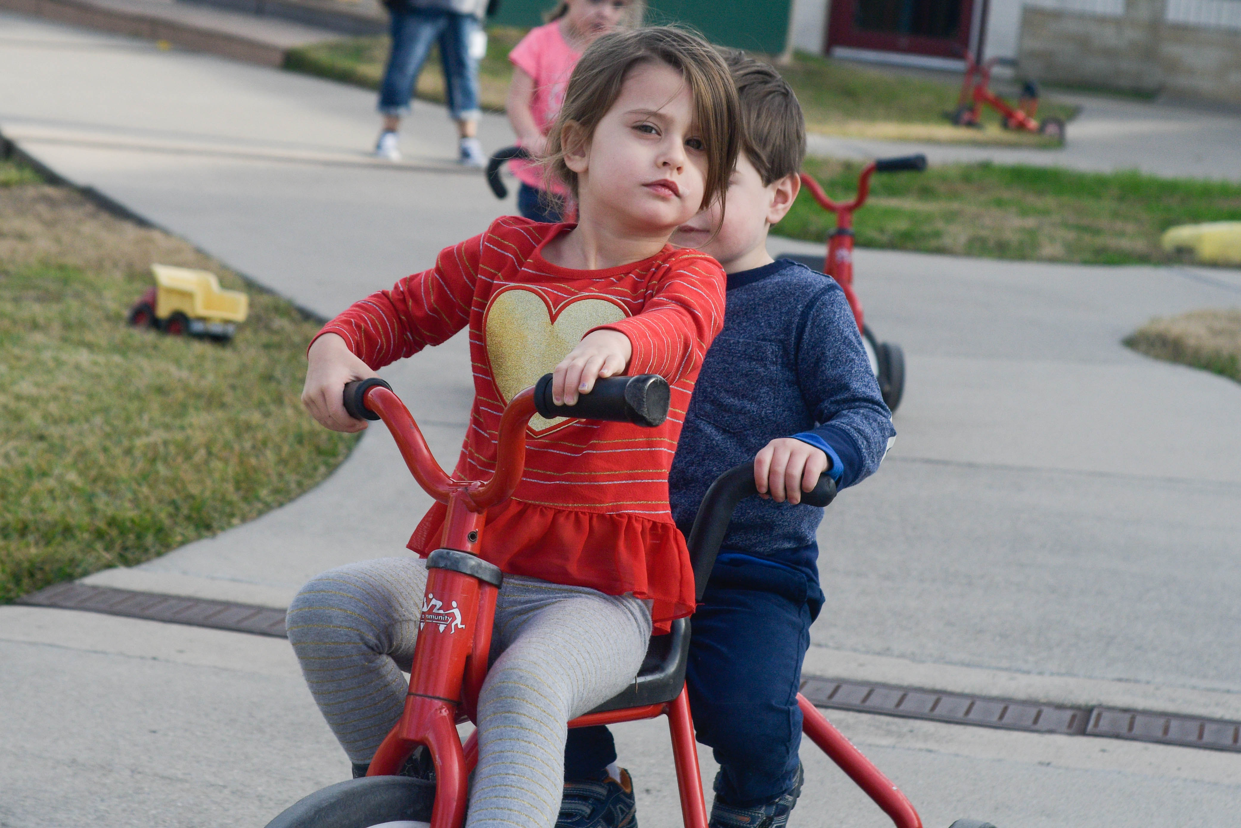 A young girl and boy ride a bicycle together outside the Center for Early Learning