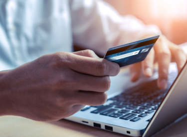 A person sitting at a laptop with a hand holding a credit card