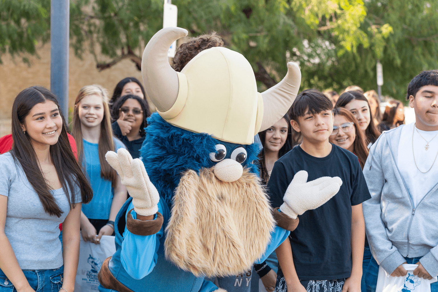 Valdar the Viking mascot poses with a group of young people outdoors.